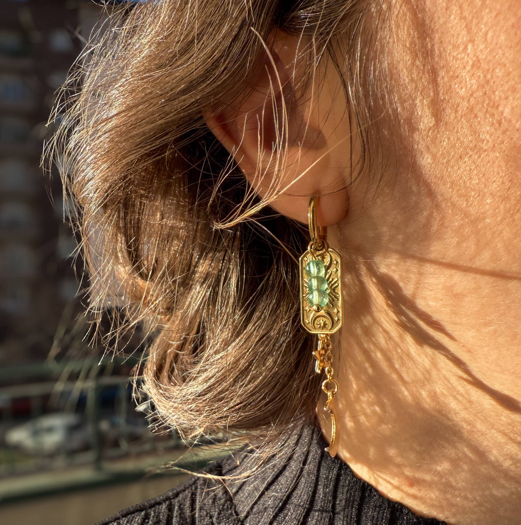 Pendientes de acero inoxidable en oro con detalle verde, colgando de la oreja, mostrando su brillo y estilo.