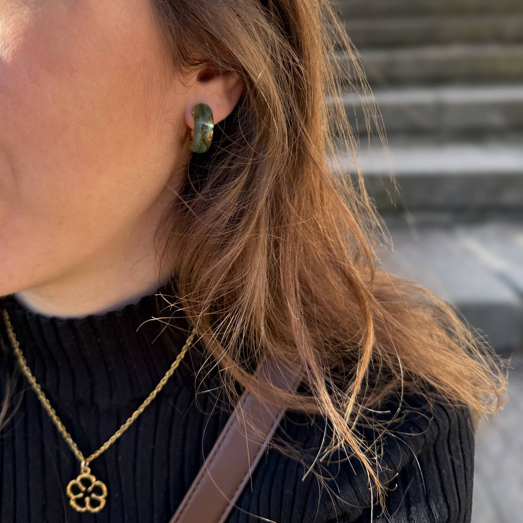 Aros Zuri de acero inoxidable y resina en una modelo con cabello suelto y una prenda de color negro.